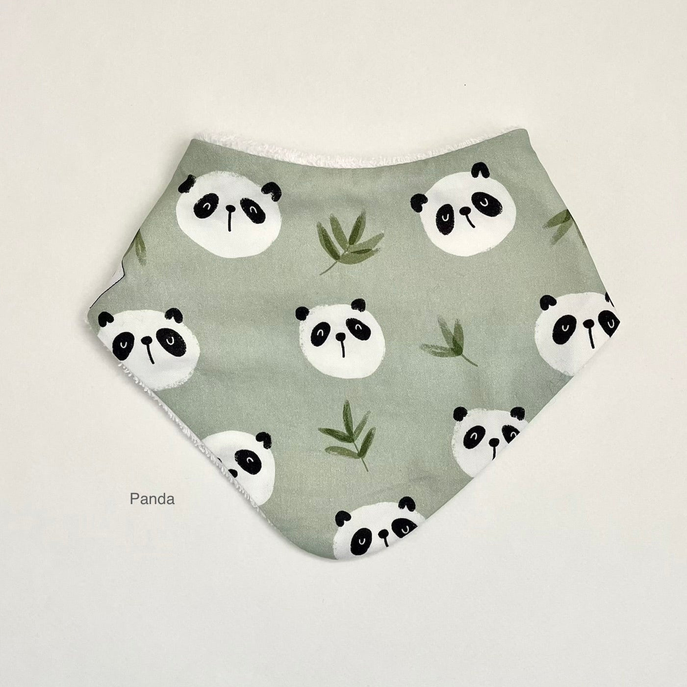 A triangular bandana bib in sage green with a repeating pattern of black and white panda faces and green bamboo leaves, displayed flat against a light off-white background.
