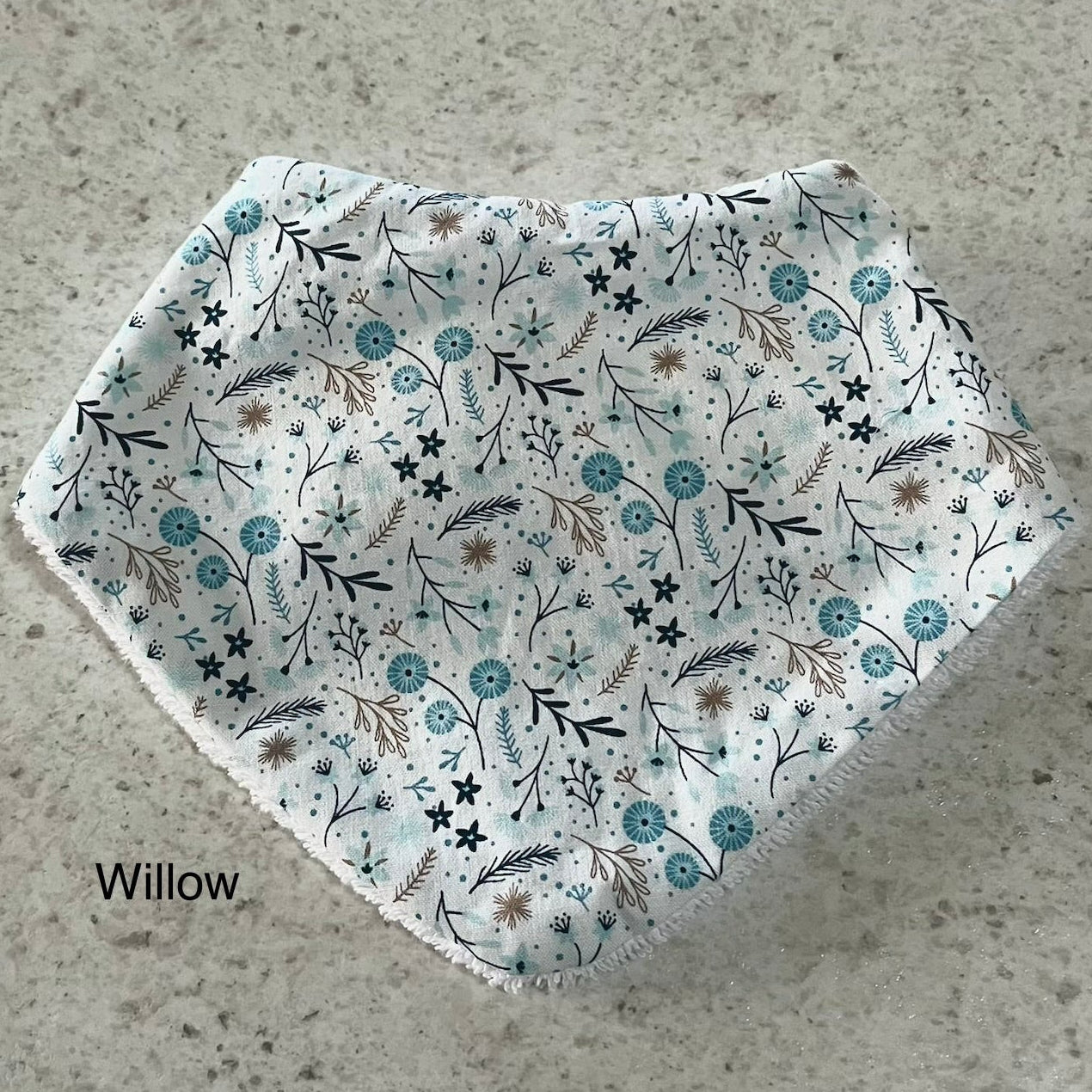 Floral patterned dribble bib with 'Willow' branding on a concrete surface