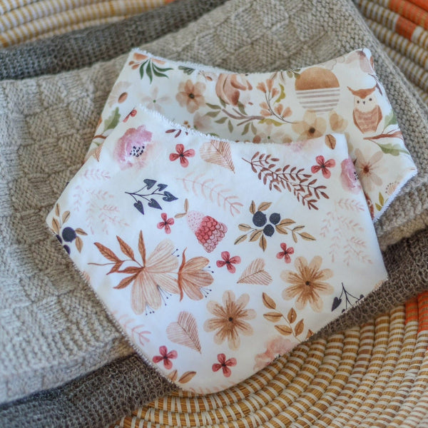 Two floral-patterned dribble bibs on a textured surface