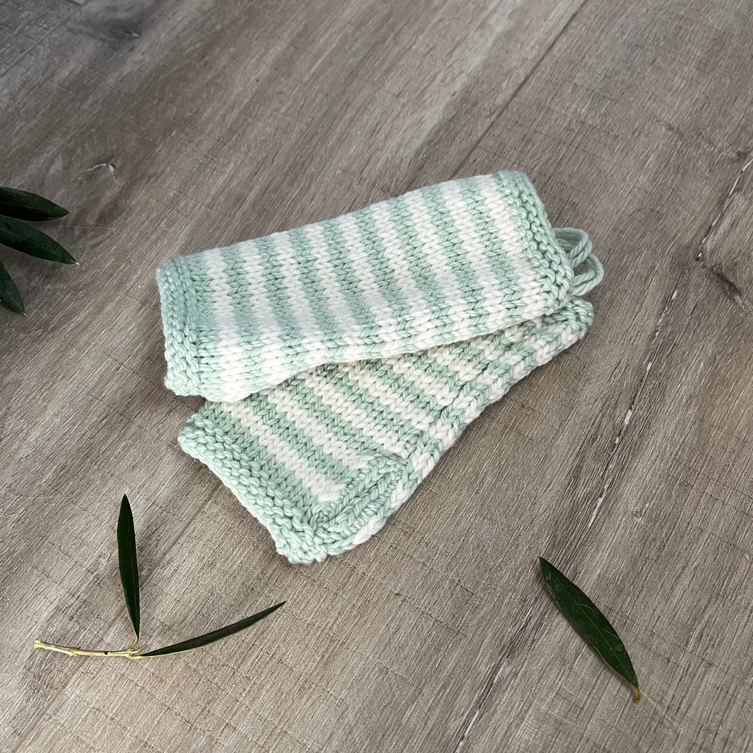 Knitted baby fingerless mittens with mint and white stripes on a wooden surface