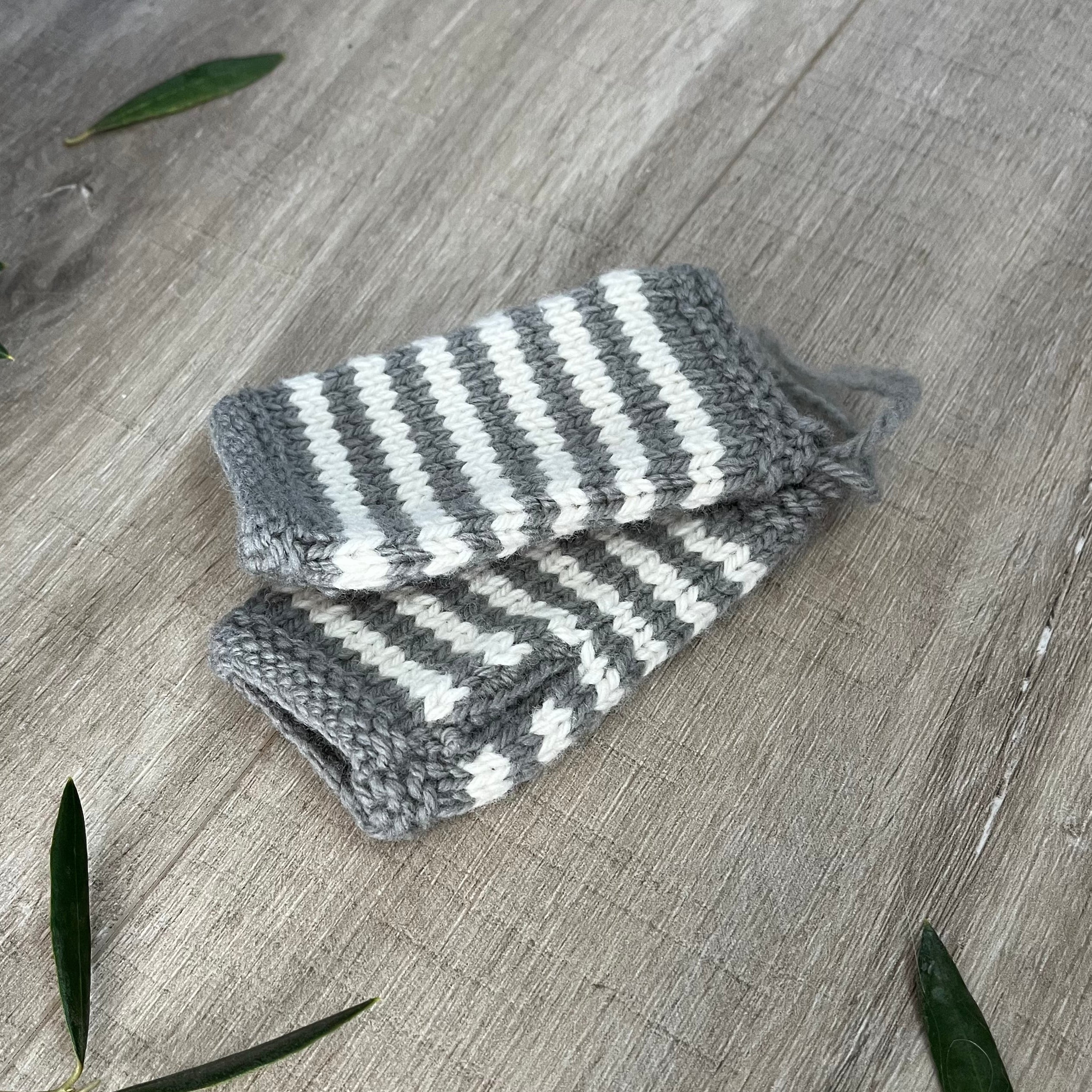 Knitted baby fingerless mittens with mushroom and white stripes on a wooden surface