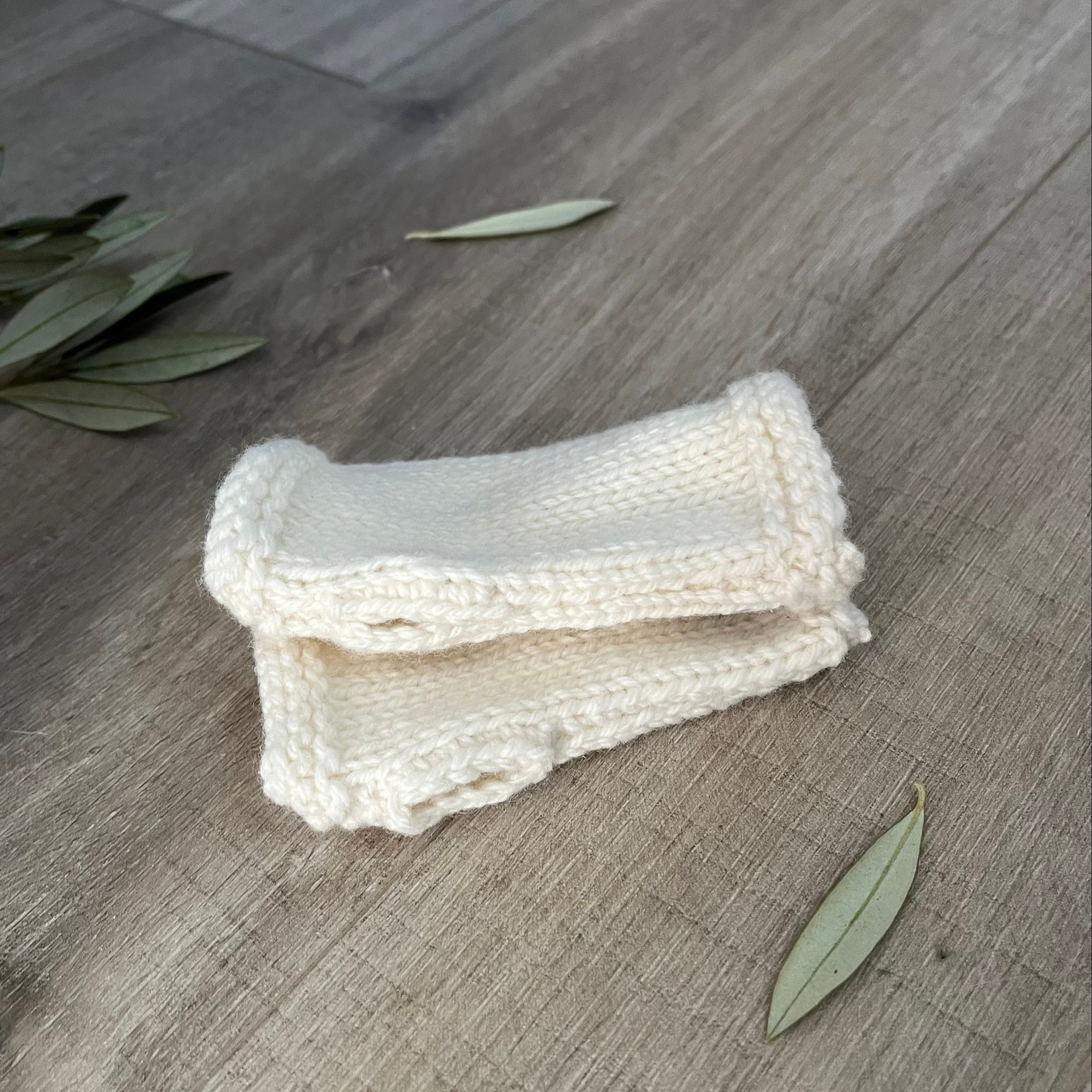Natural knitted fingerless mittens on a wooden surface with olive leaves.