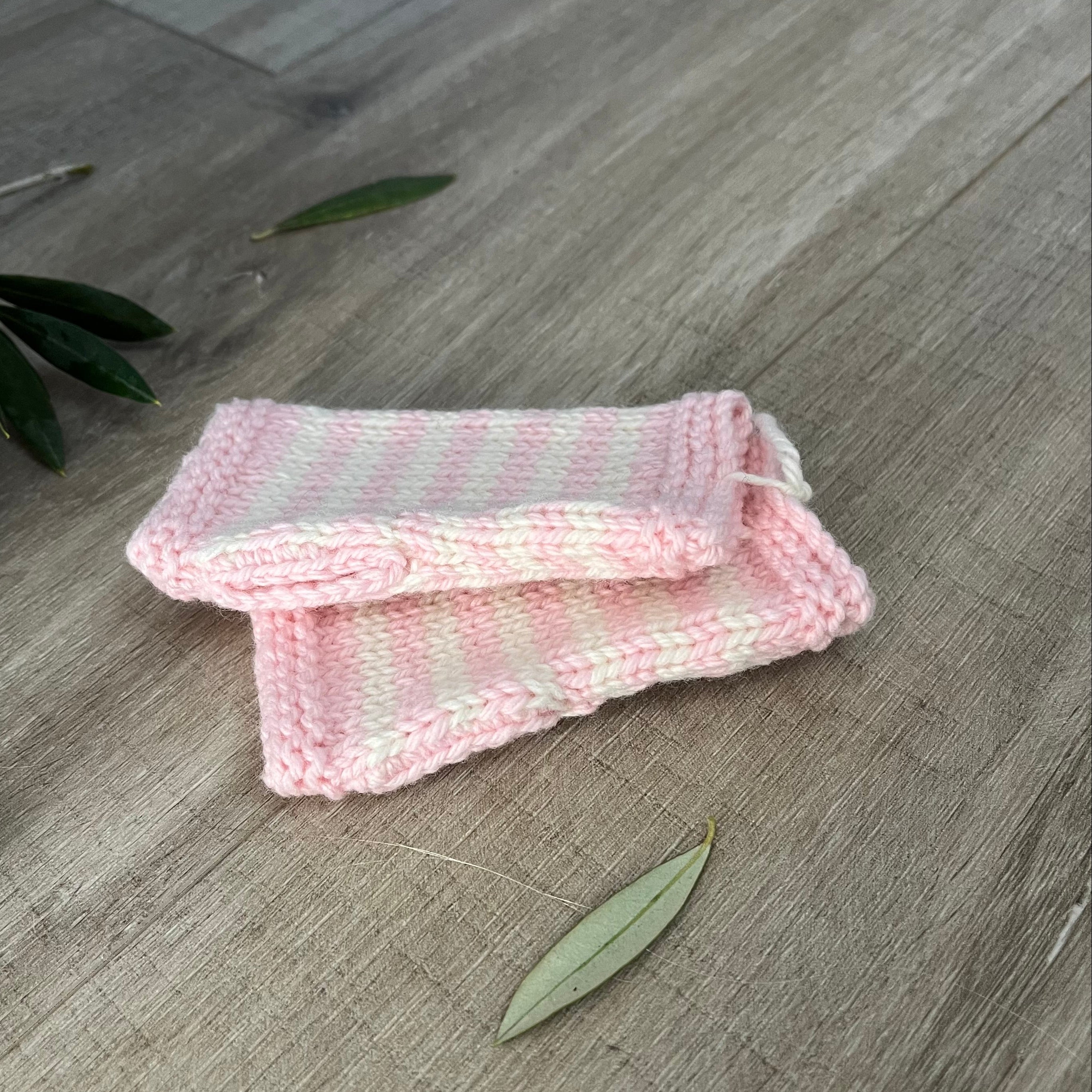 Knitted baby fingerless mittens with pink and white stripes on a wooden surface
