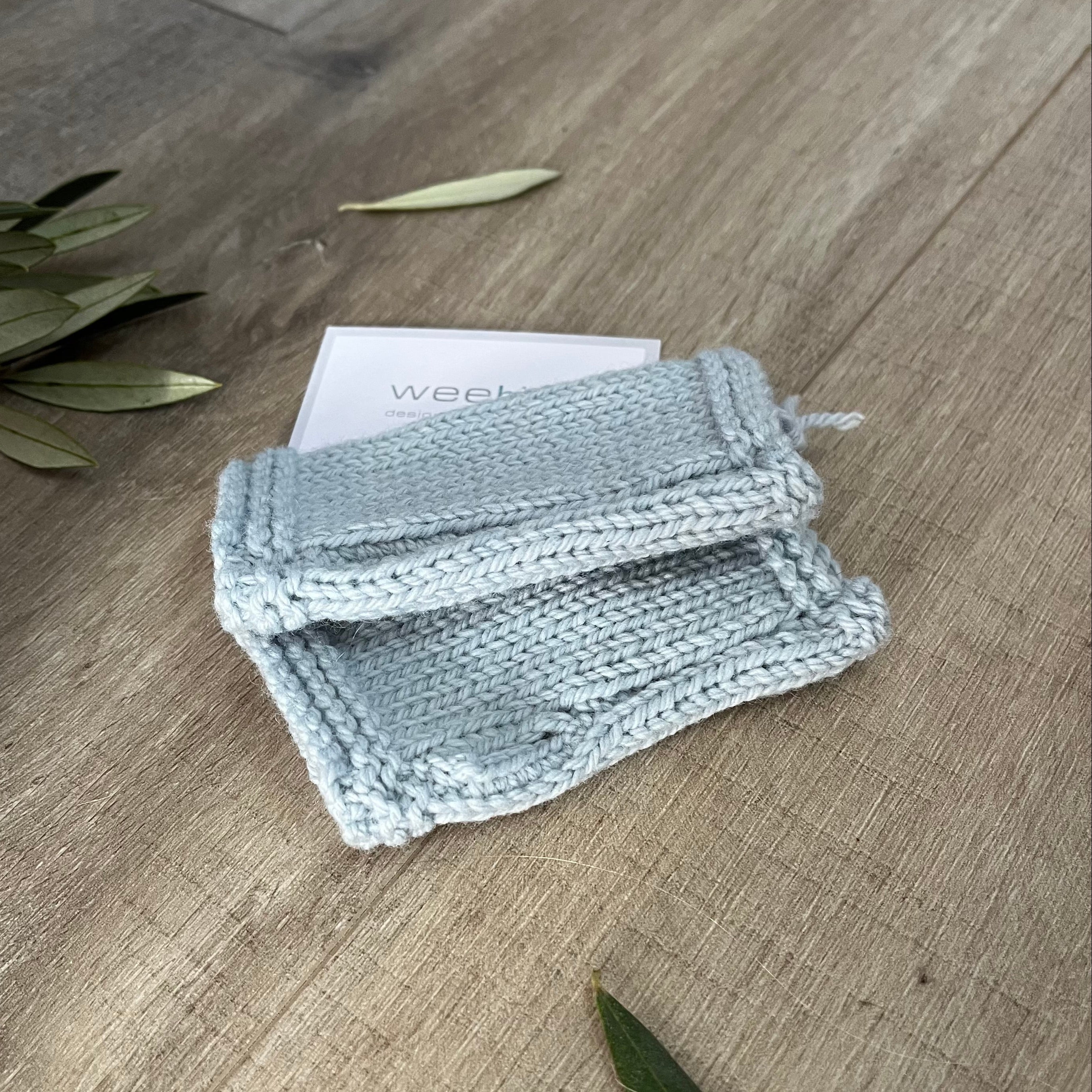 Blue knitted fingerless mittens on a wooden surface with olive leaves.