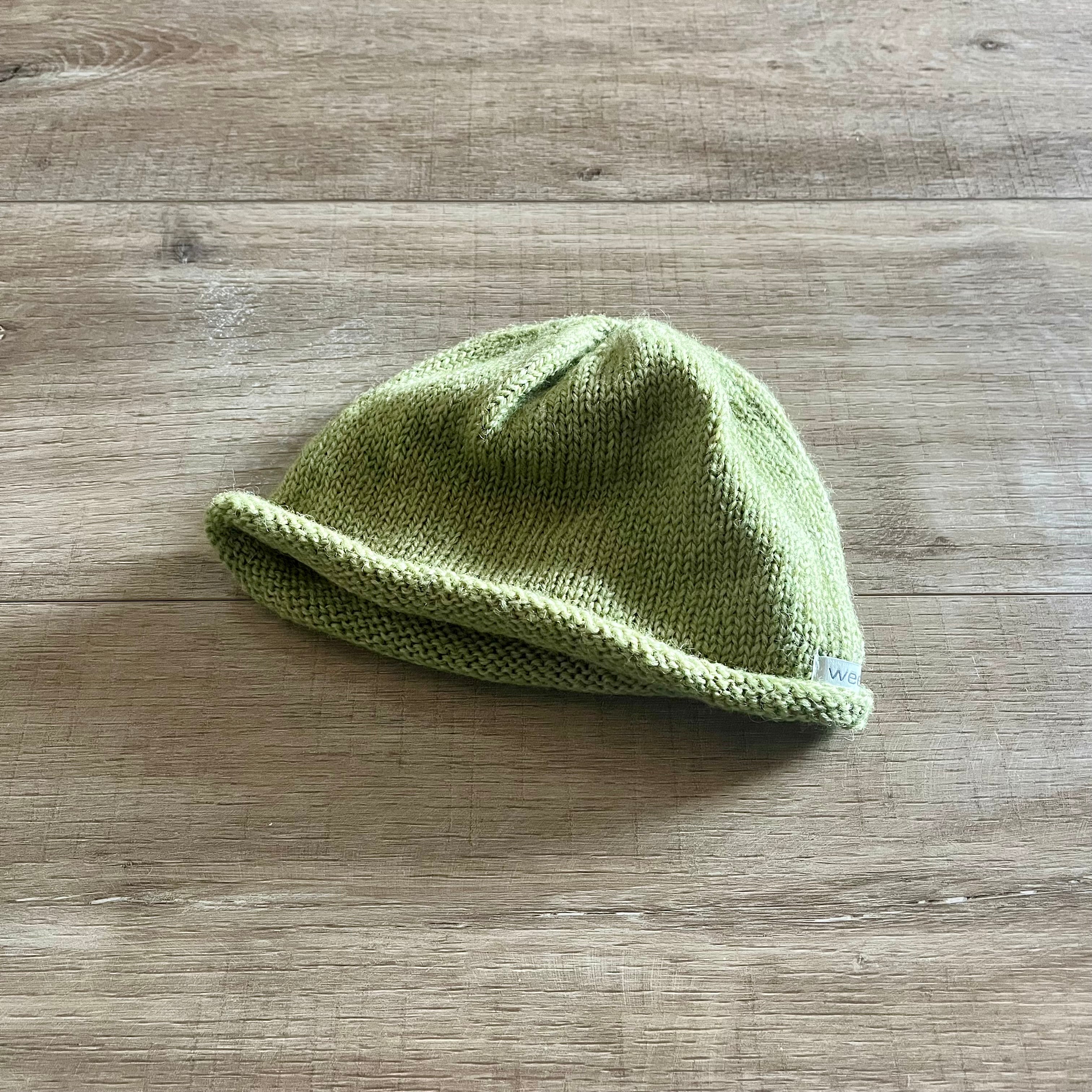 Green knitted baby hat on a wooden surface