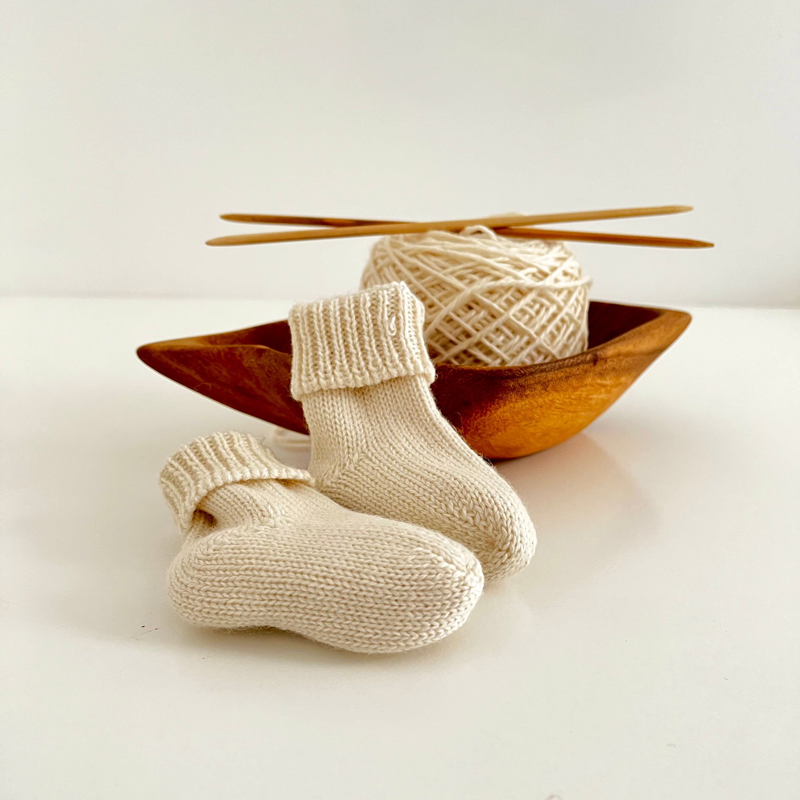 Knitted baby socks with yarn and knitting needles on a white background