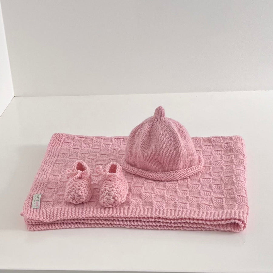 Knitted pink baby travel rug beanie and bootie set on white shelf