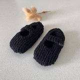 Pair of black knitted baby shoes on a light gray background