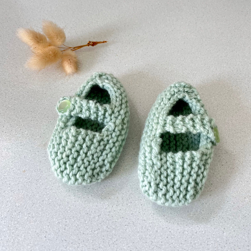Pair of green knitted baby shoes on a light grey background