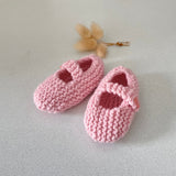 Pair of pink knitted baby shoes on a light grey background