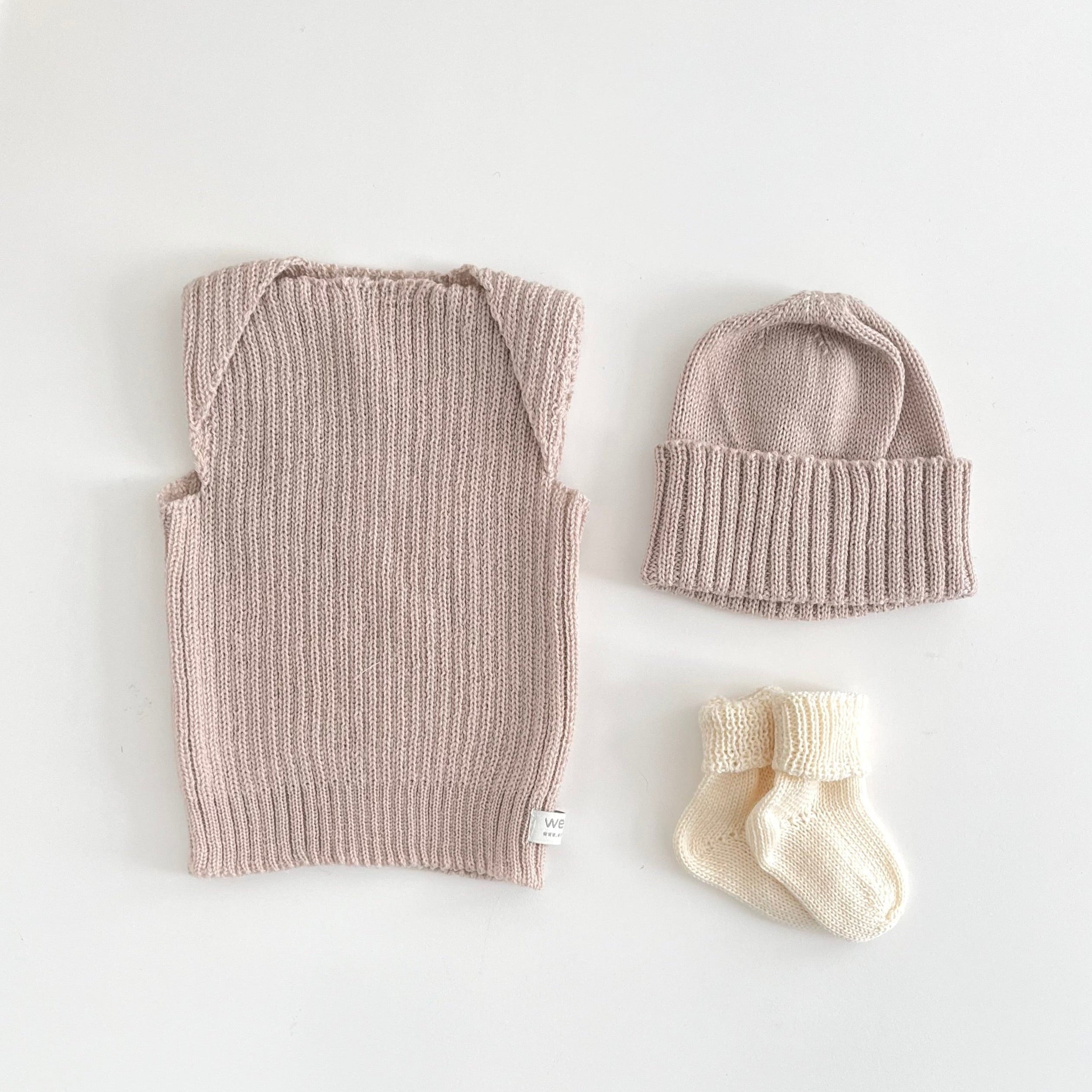 Knitted baby outfit with hat and socks on a light background