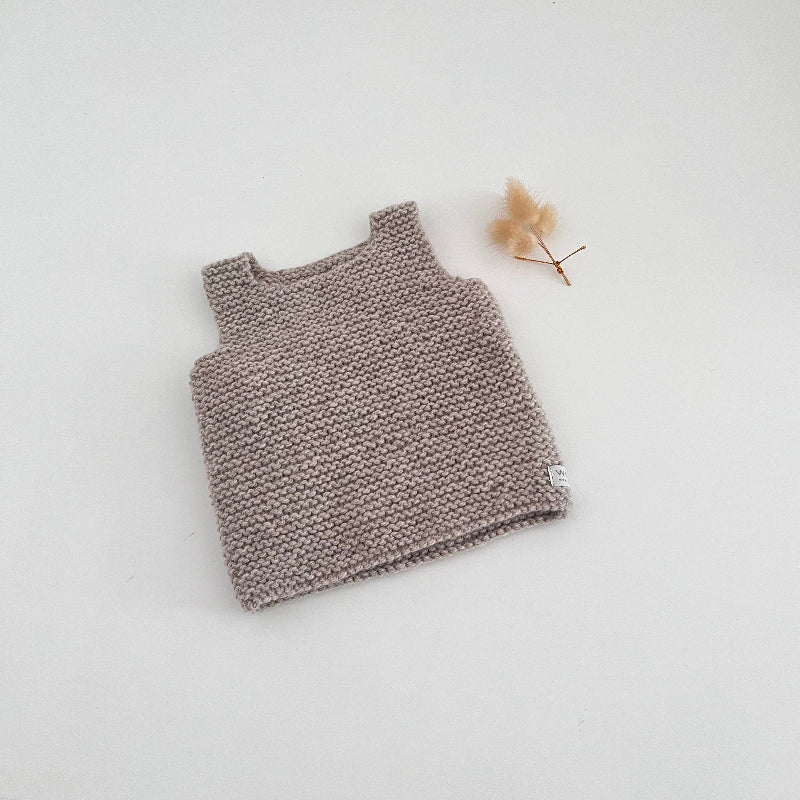 Knitted tank top on a light gray background with a small dried flower.