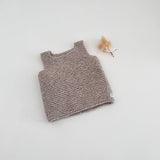 Knitted tank top on a light gray background with a small dried flower.
