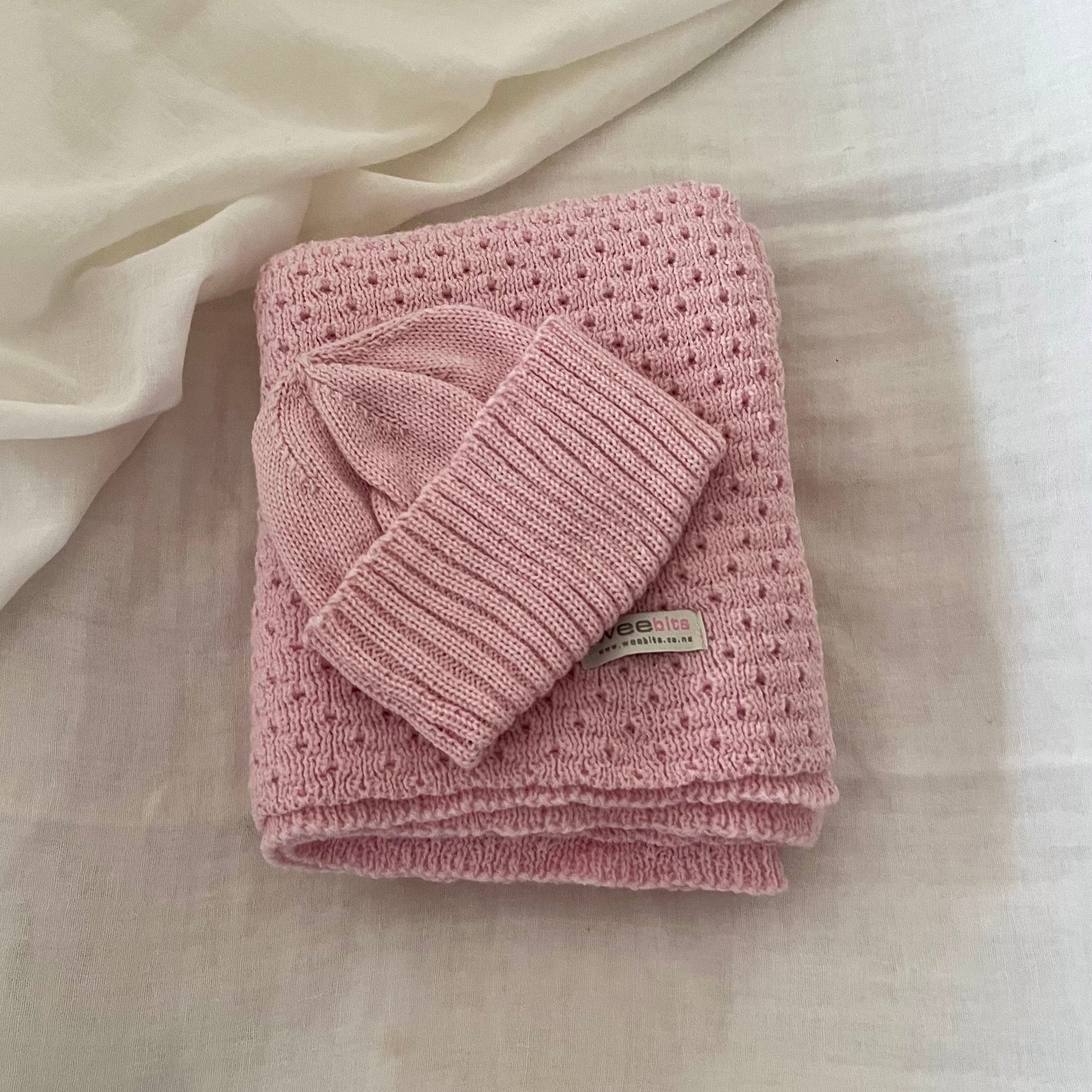 Folded pink baby wrap with a matching beanie on a light fabric background