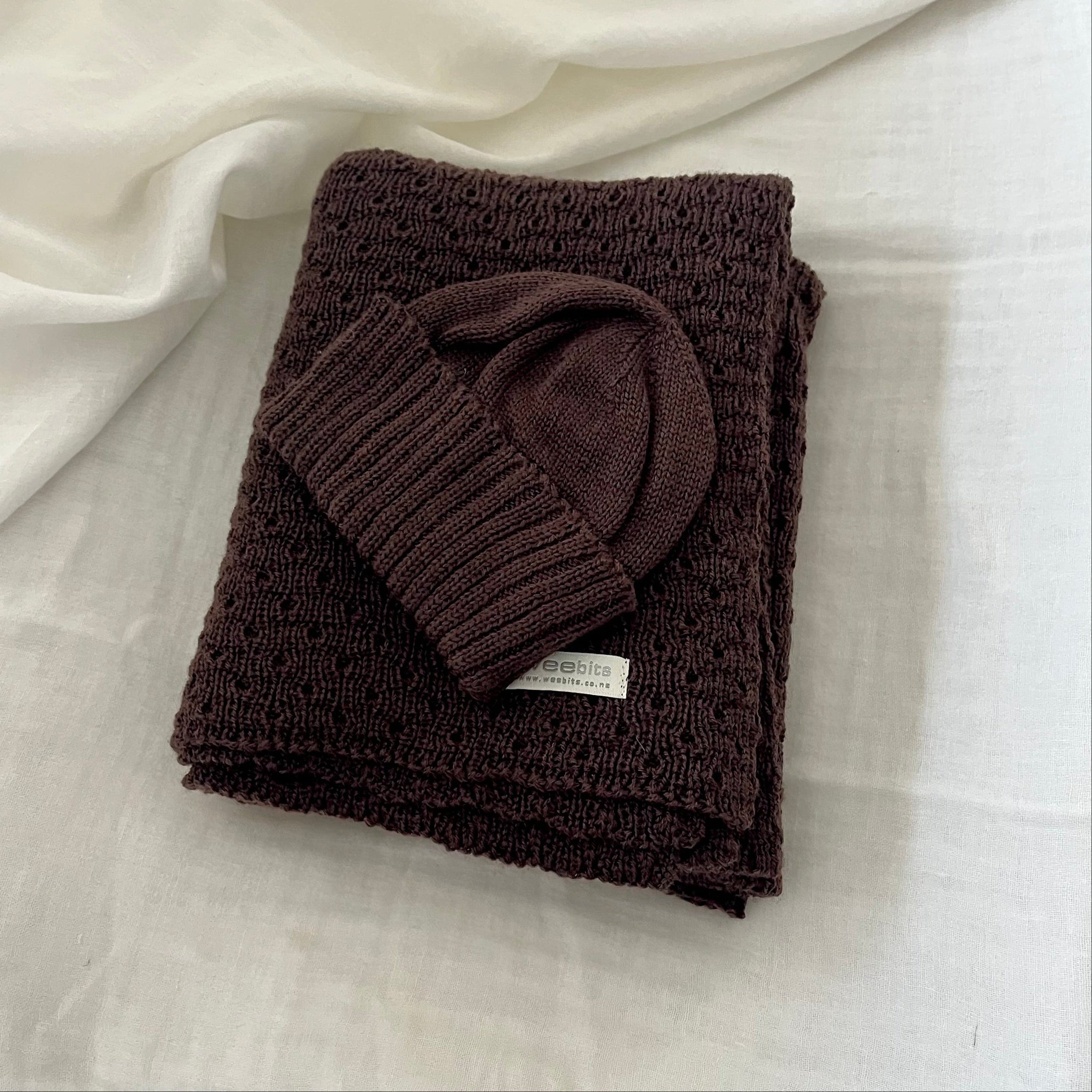 Folded brown baby wrap with a matching beanie on a light fabric background