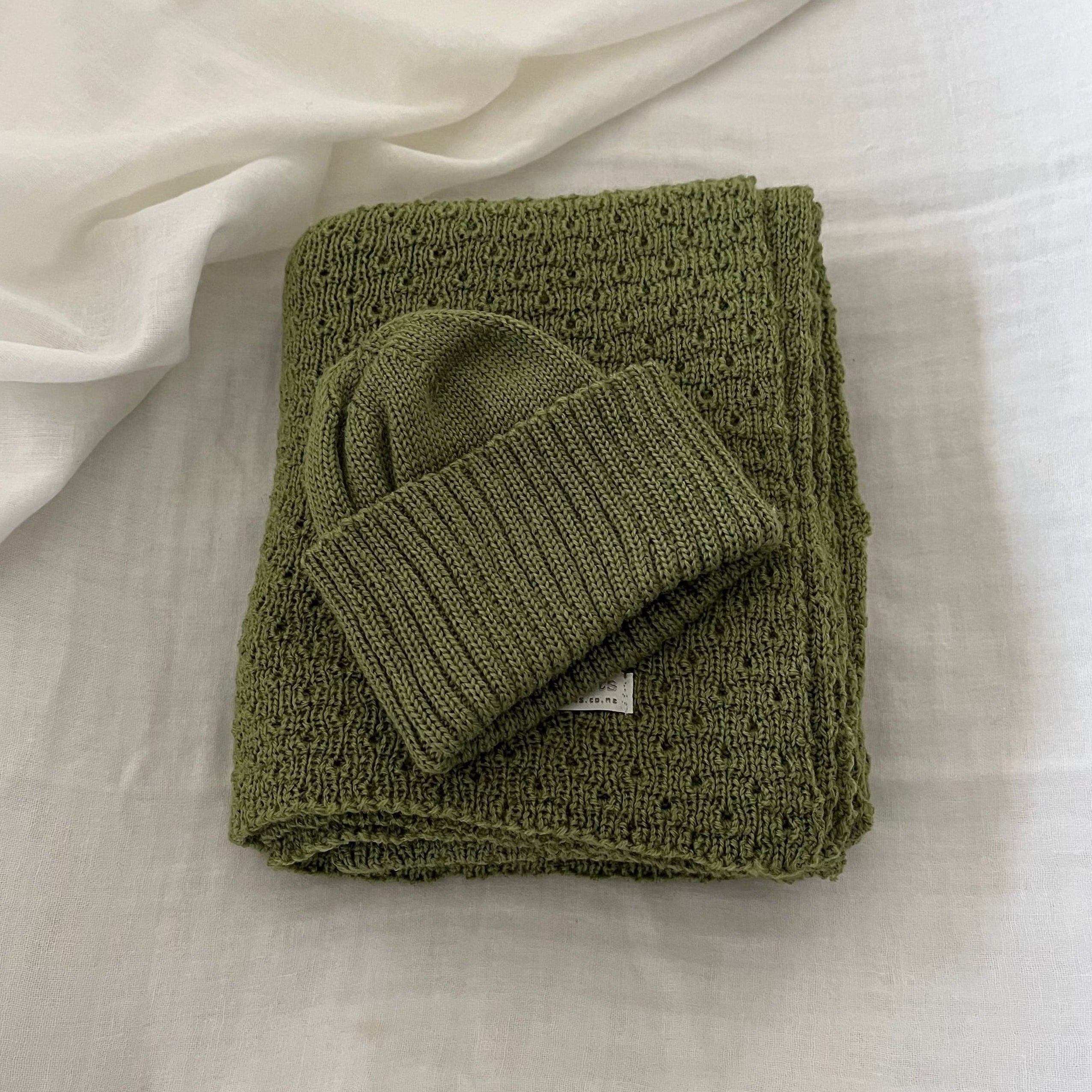 Folded moss baby wrap with a matching beanie on a light fabric background