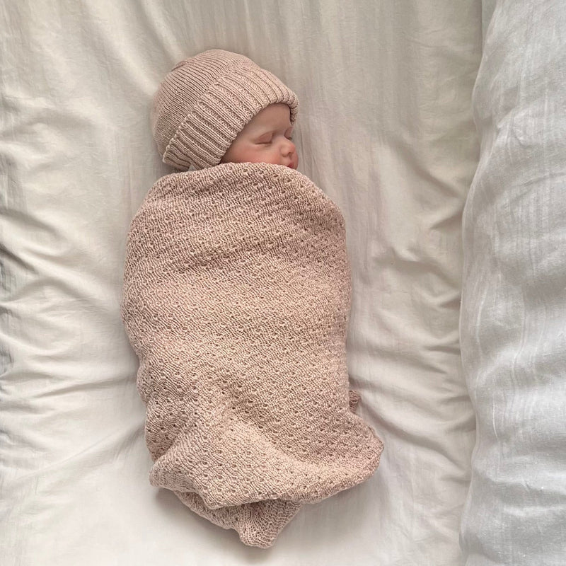 Newborn baby swaddled in a sandstone blanket and hat on a white background