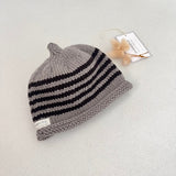 Mushroom and chocolate striped knit baby hat with a tag on a light grey background