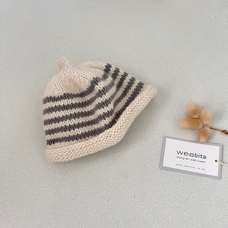 Natural and mushroom striped knit baby hat with a tag on a light grey background