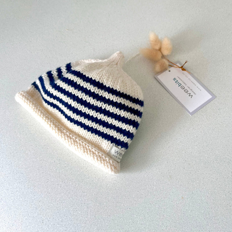 Natural and navy striped knit baby hat with a tag on a light grey background