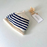 Natural and navy striped knit baby hat with a tag on a light grey background