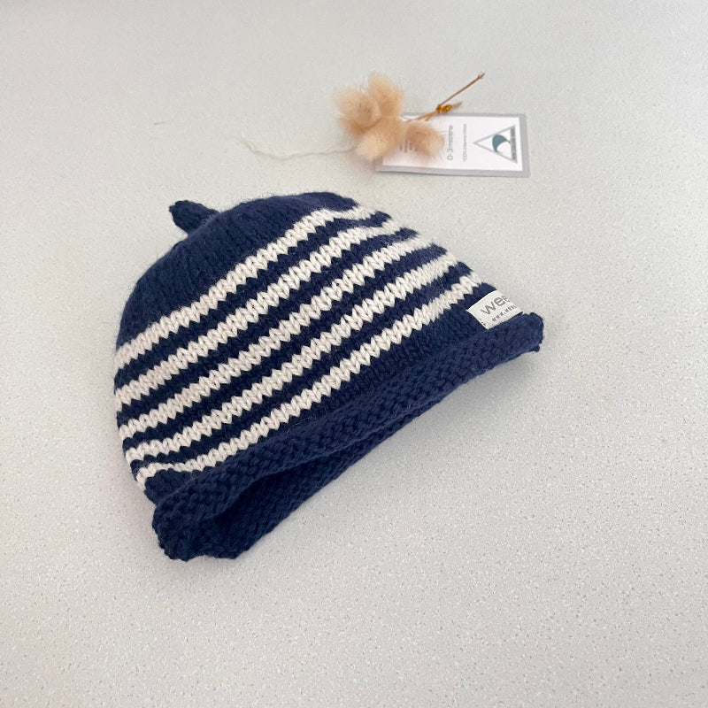 Navy and natural striped knit baby hat with a tag on a light grey background