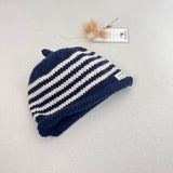 Navy and natural striped knit baby hat with a tag on a light grey background