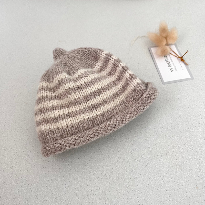 Oatmeal and natural striped knit baby hat with a tag on a light grey background