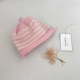 Pink and natural striped knit baby hat with a tag on a light grey background