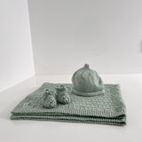 Mint baby hat and booties set on a folded green blanket against a white background