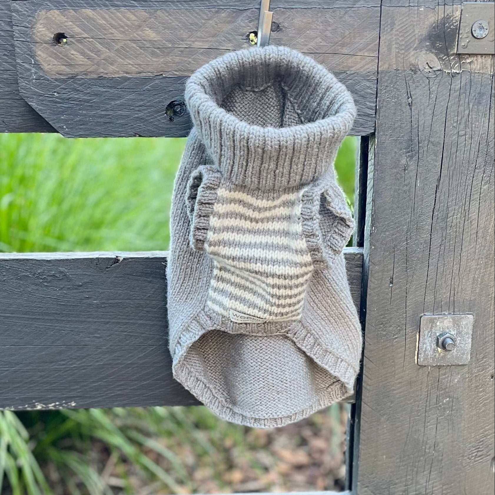 A small Weebits merino dog jumper hanging from a hook on a rustic wooden fence.