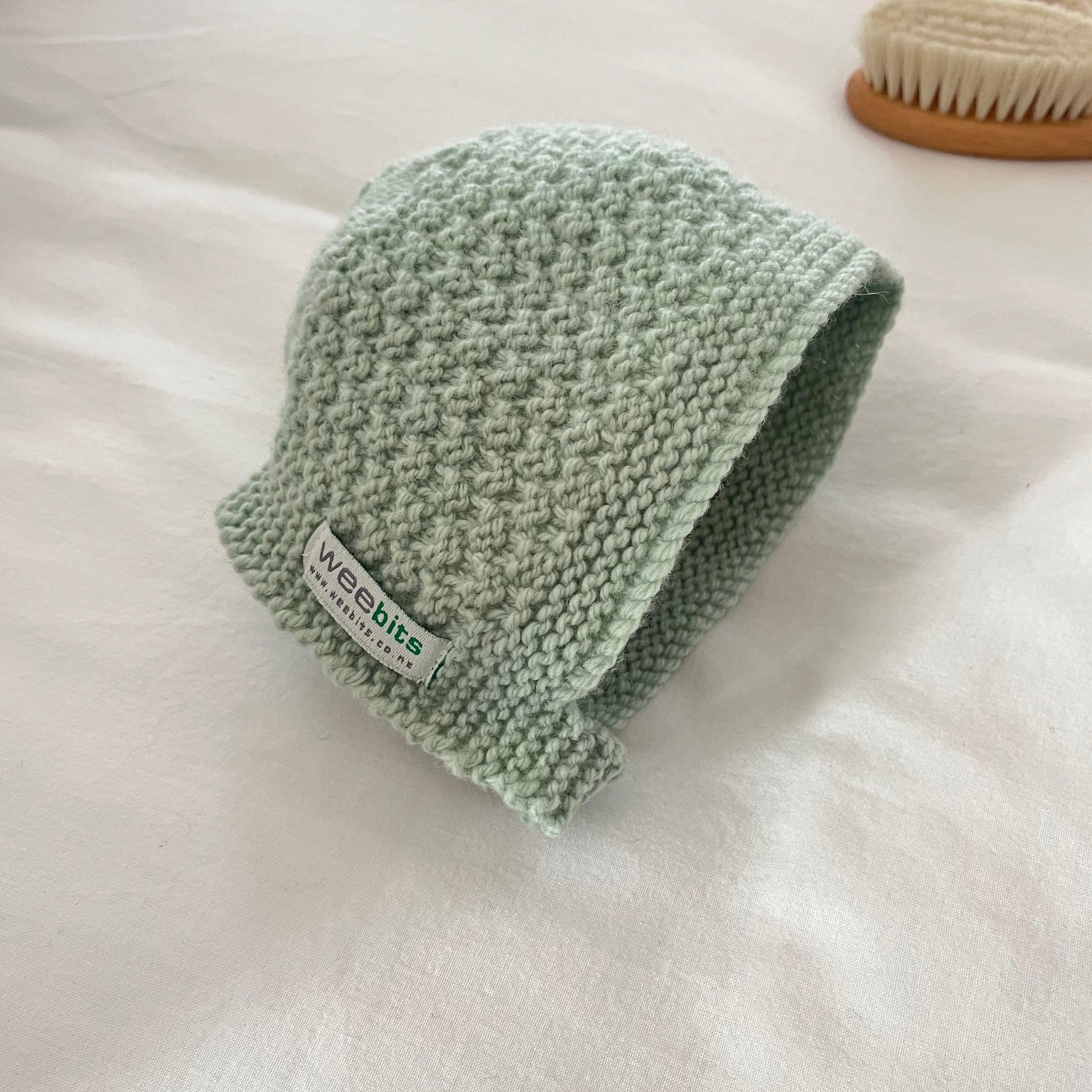 Knitted green baby hat with 'weebits' label on a white background