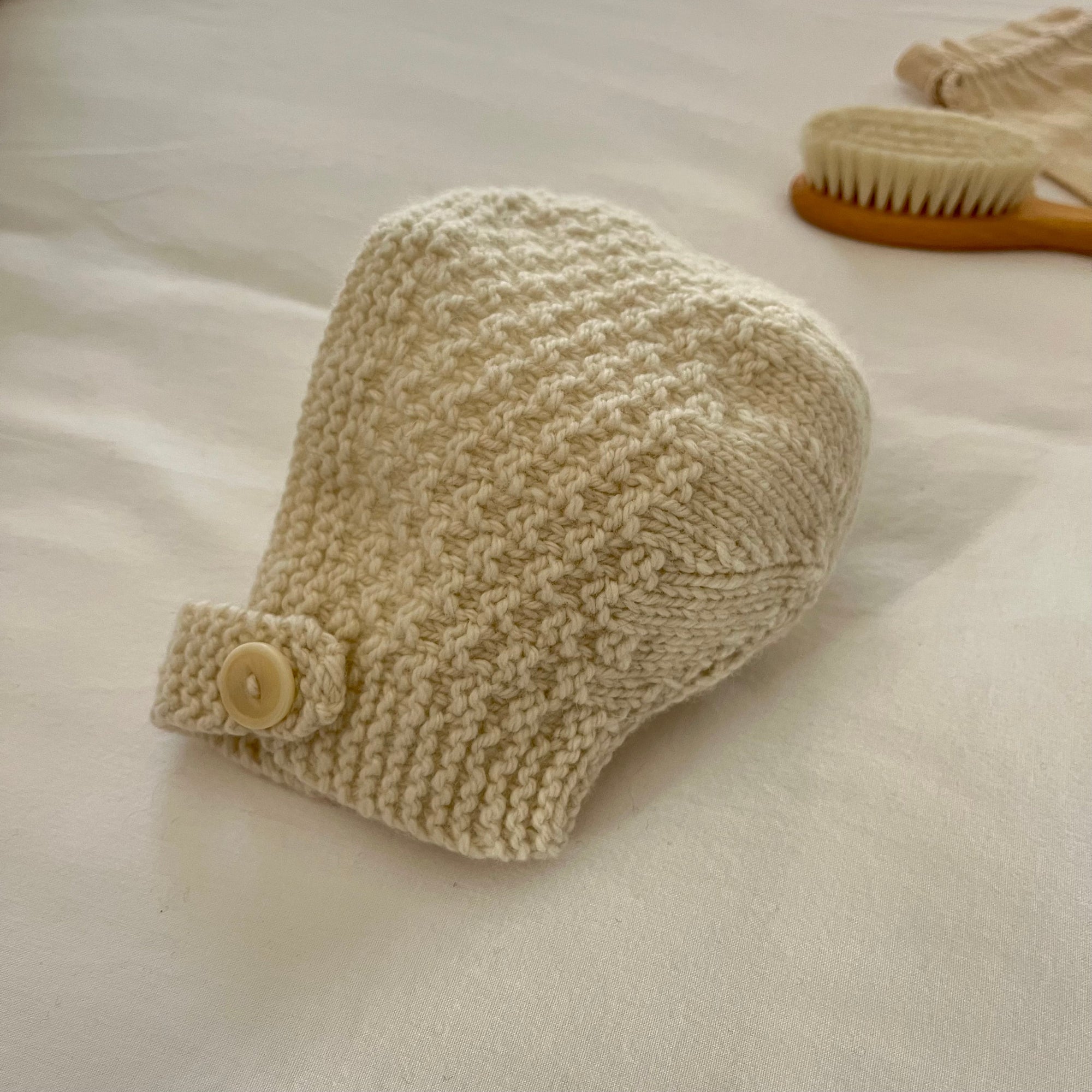 Knitted baby bonnet with a button on a light background