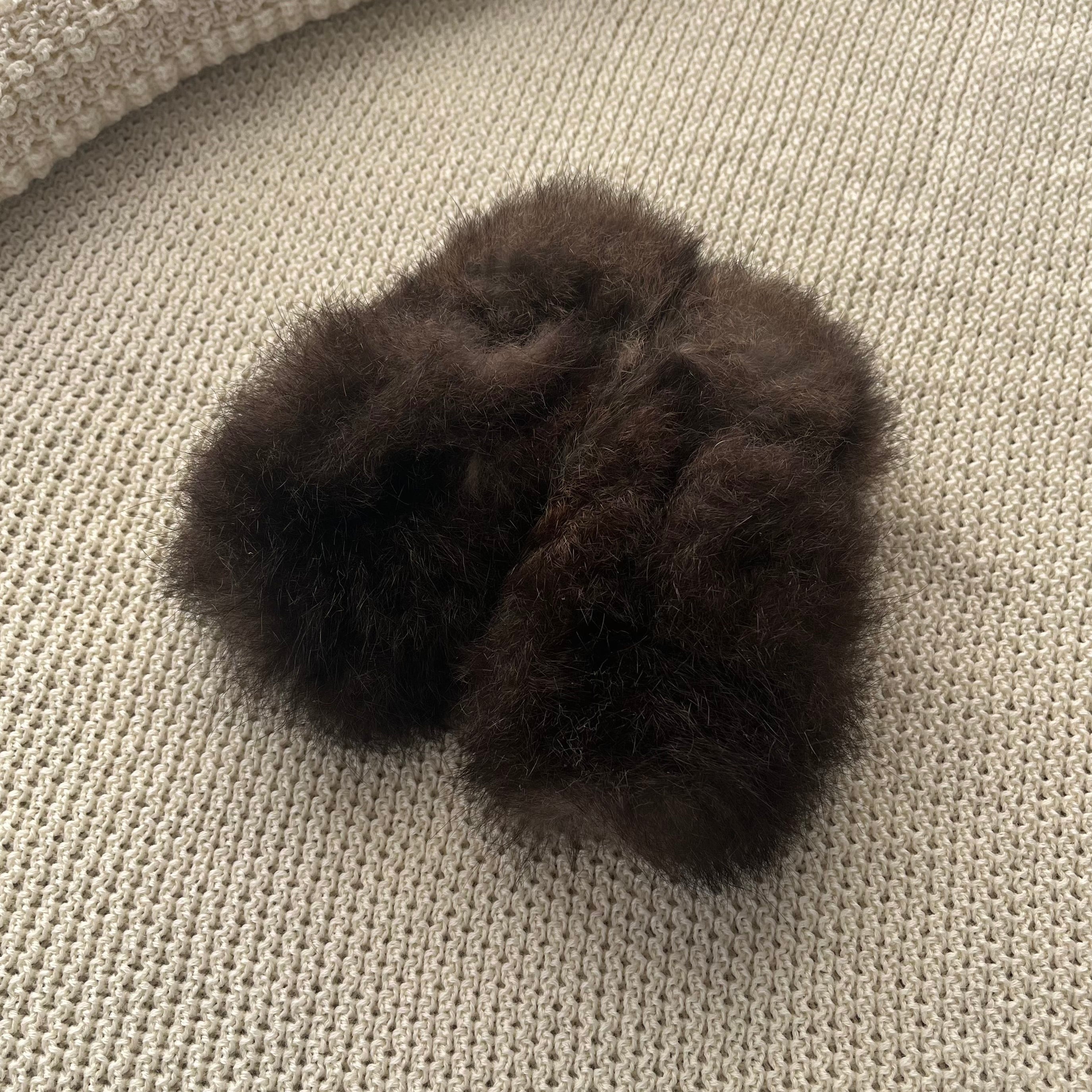 Two dark grey possum booties on a textured beige surface