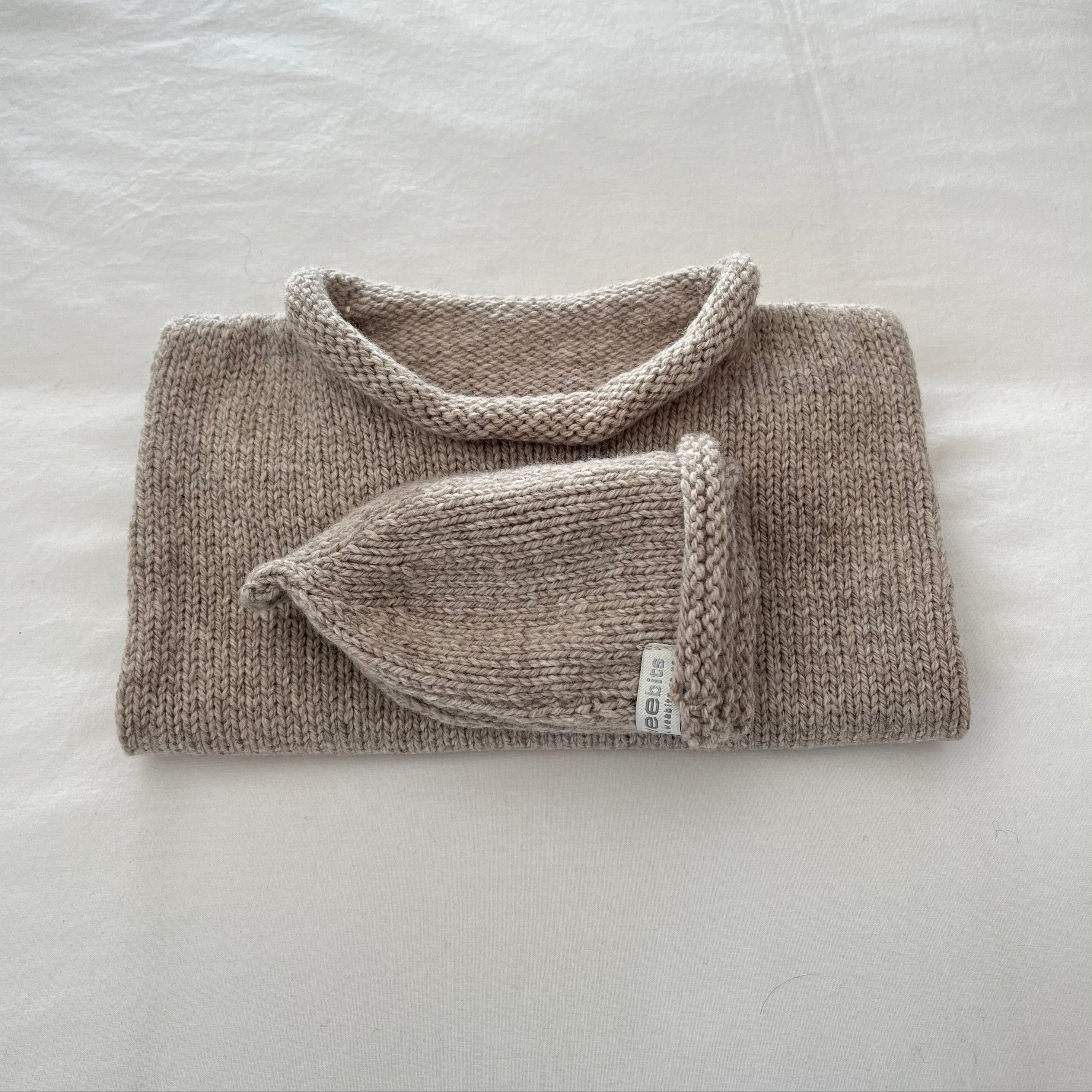 Folded oatmeal knit baby vest and beanie on a light surface