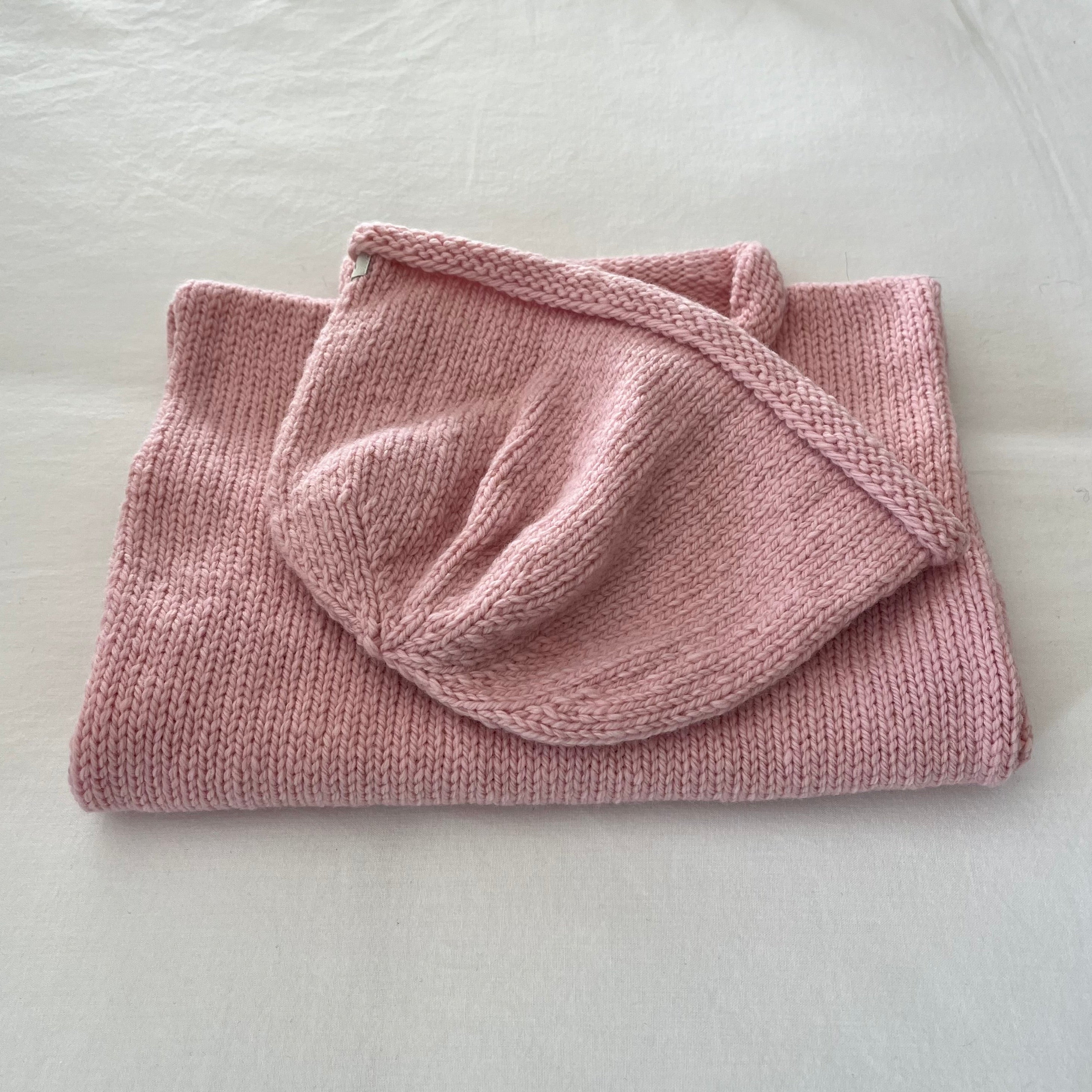 Folded pink knitted vest and beanie on a light gray surface