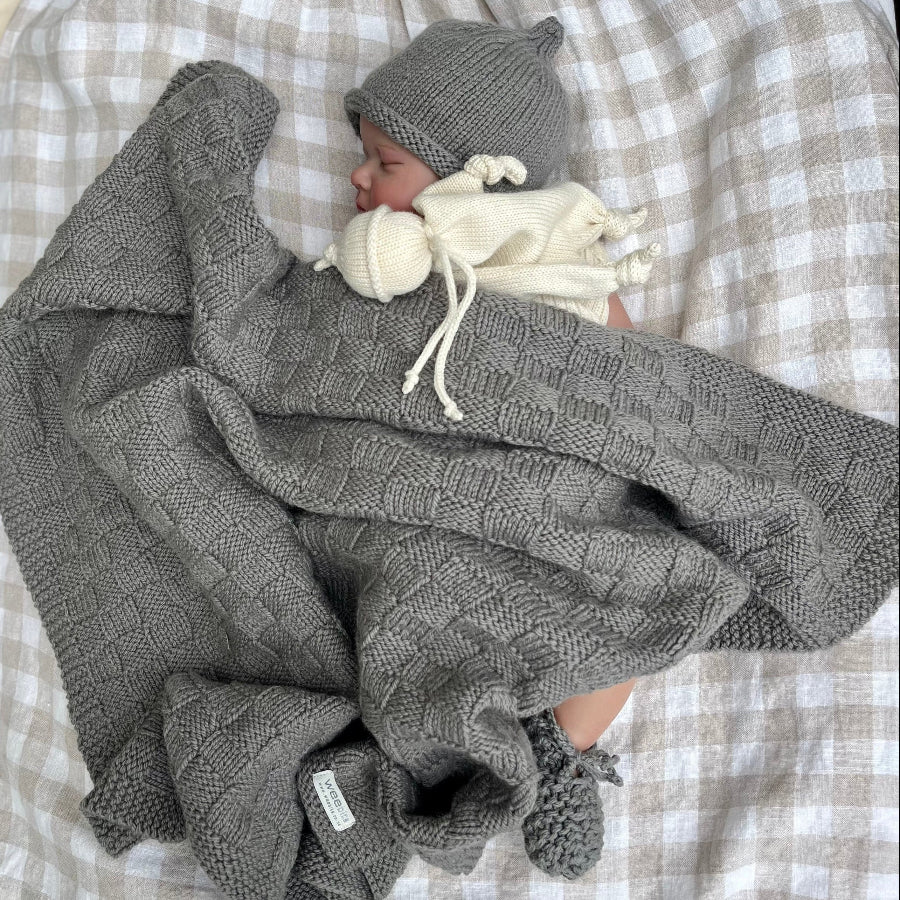 Sleeping baby in mushroom travel rug, beanie and booties on gingham blanket