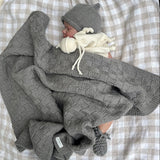 Sleeping baby in mushroom travel rug, beanie and booties on gingham blanket