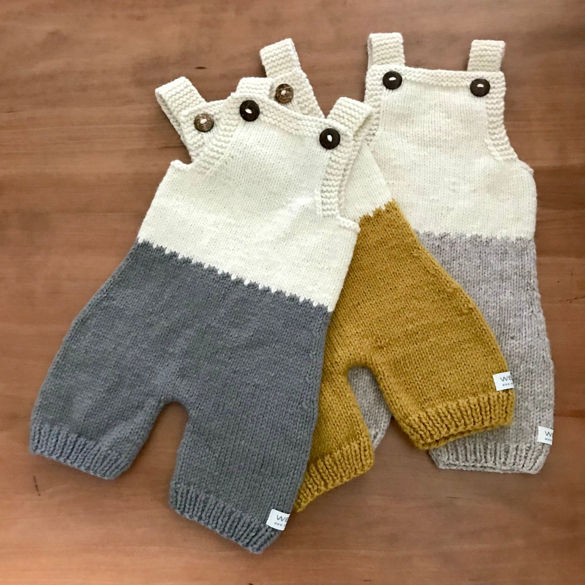 Two merino knitted overalls in gray, yellow, and white on a wooden surface