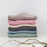 Stack of folded sweaters in various colours on a white surface