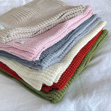 Stack of folded knitted blankets in various colors on a white surface