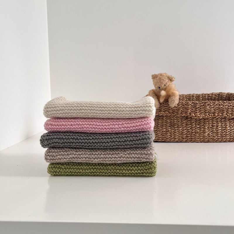 Stack of coloured tank tops wit teddy in basket