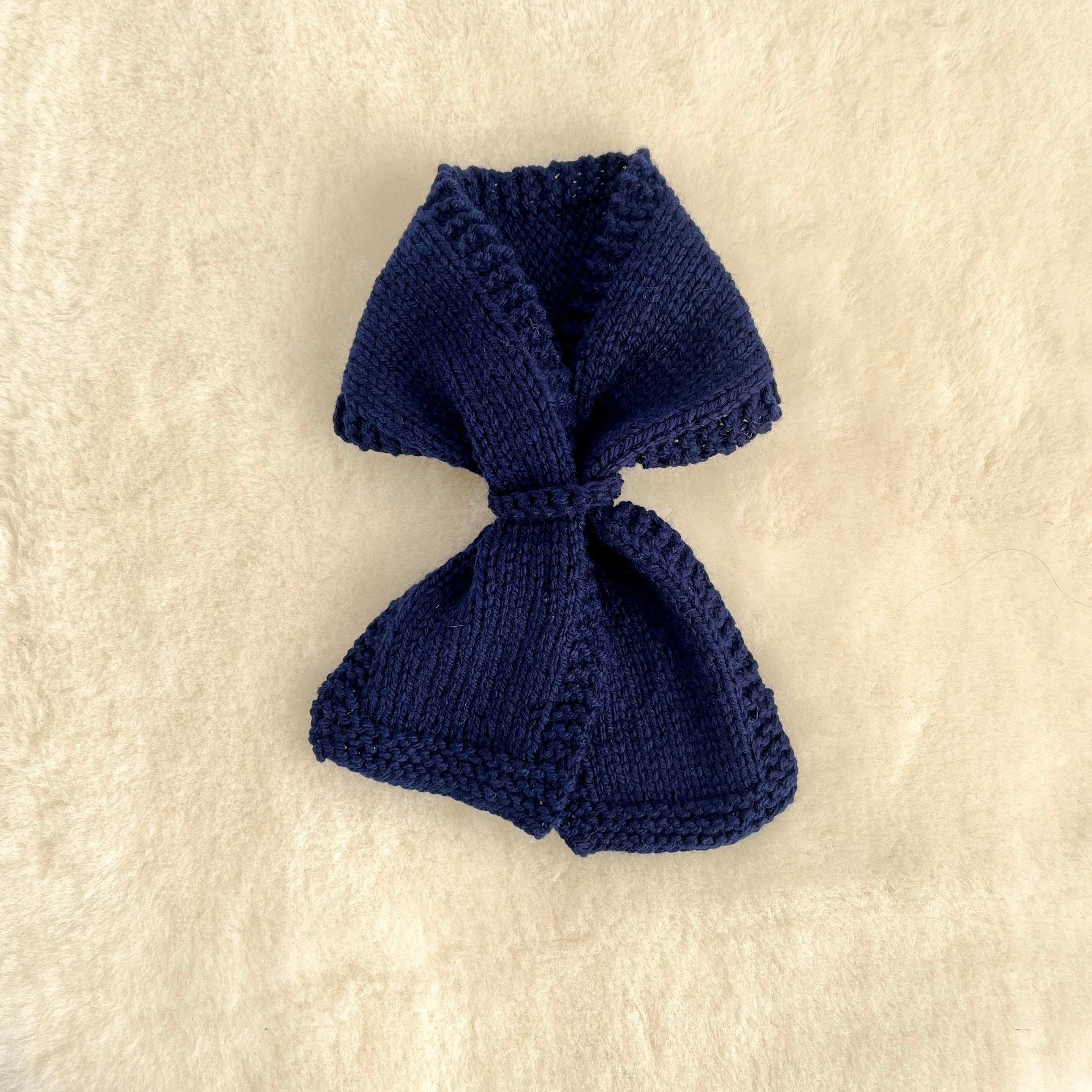 A small knitted loop scarf in navy laid flat on a textured cream-colored fabric background.