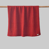 Textured burnt orange bassinet blanket hanging on a wooden rod against a grey background