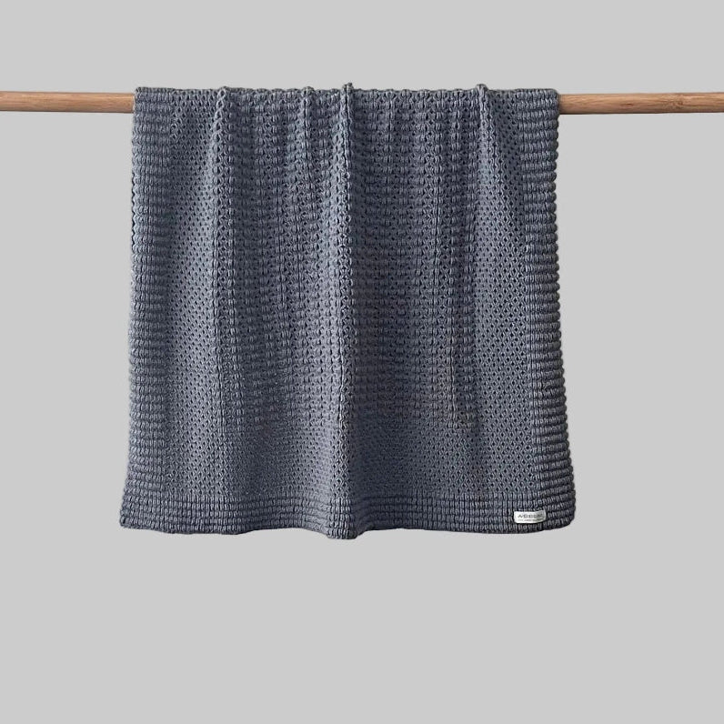 Textured dustky blue bassinet blanket hanging on a wooden rod against a grey background