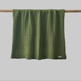 Textured moss bassinet blanket hanging on a wooden rod against a grey background
