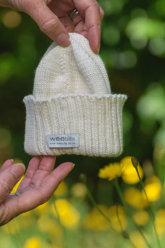 Small natural knitted beanie with 'weebits' label held by a hand against a blurred natural background