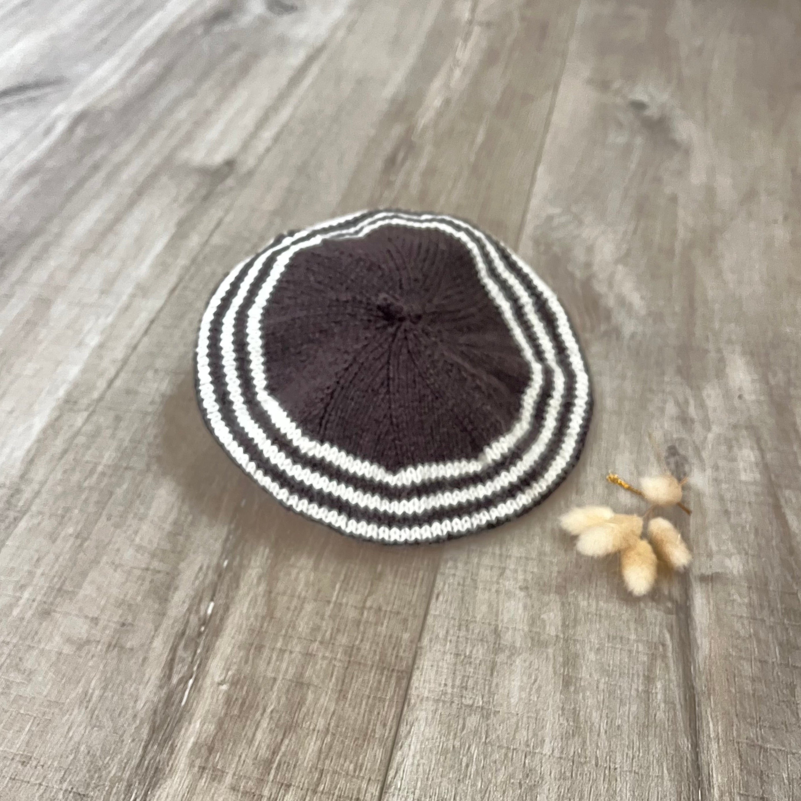 Knitted beret with chocolate and white stripes on a wooden surface