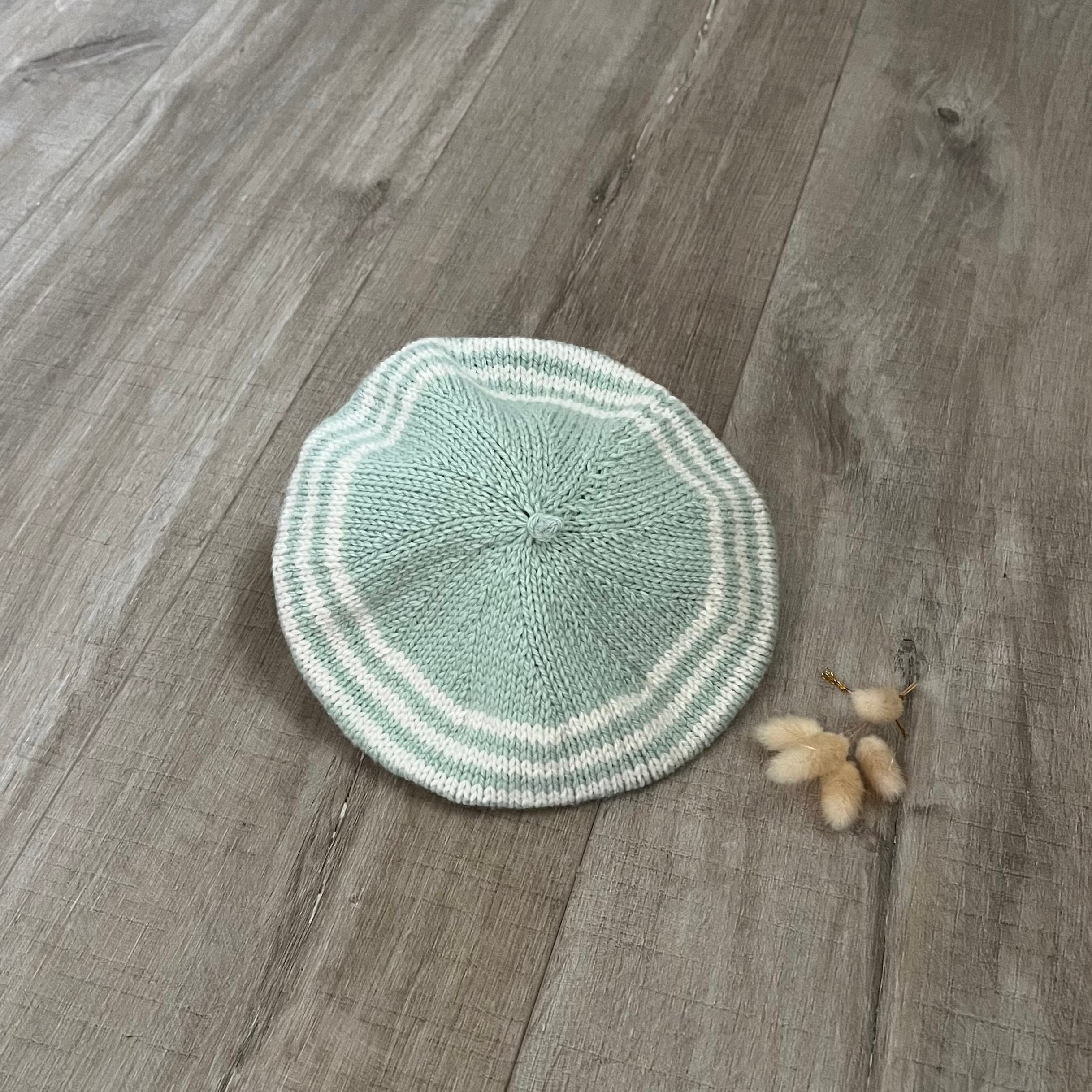 Knitted green stripe beret on a wooden surface 