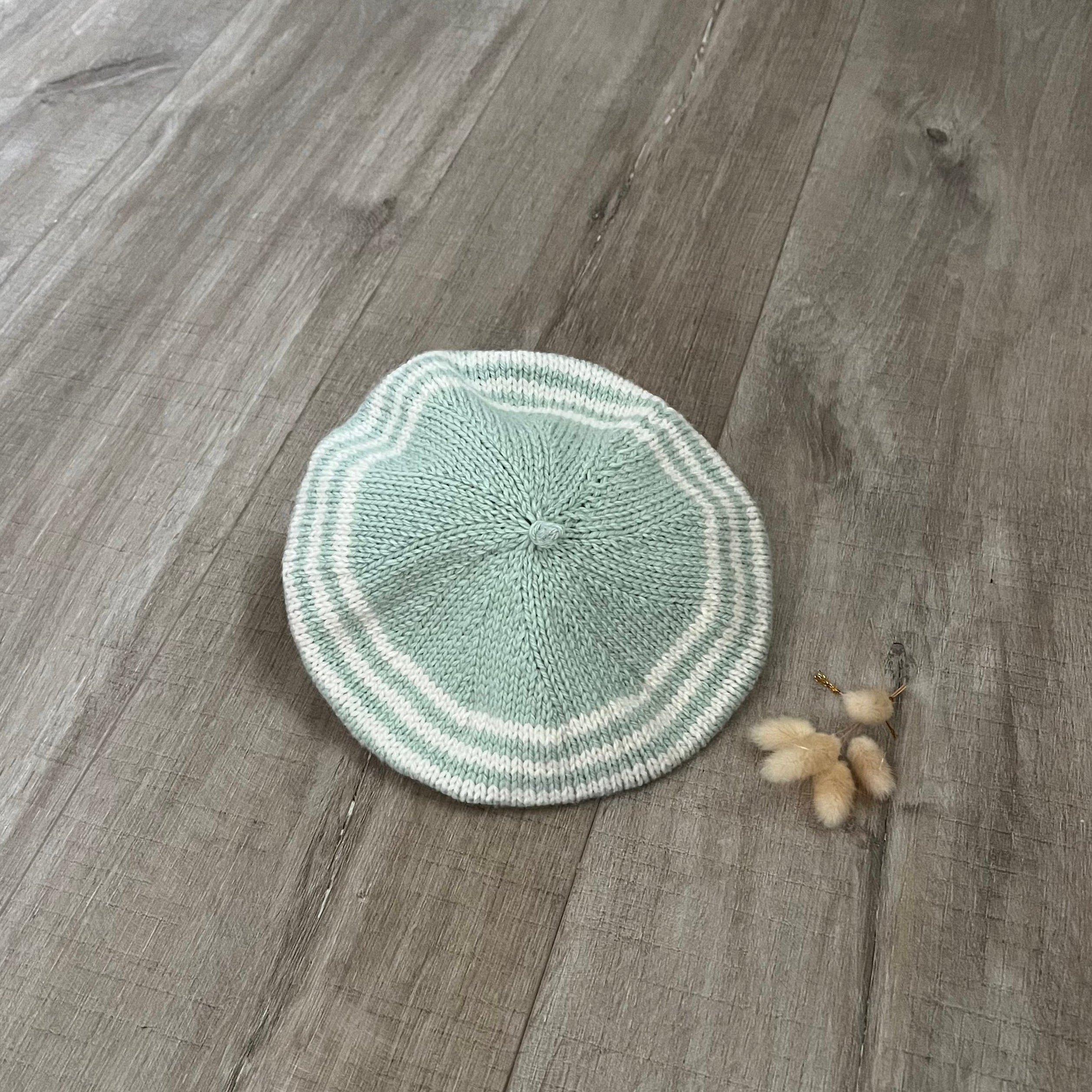 Knitted green stripe beret on a wooden surface 